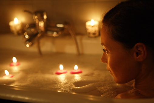 Woman relaxing in candle lit bath, side view